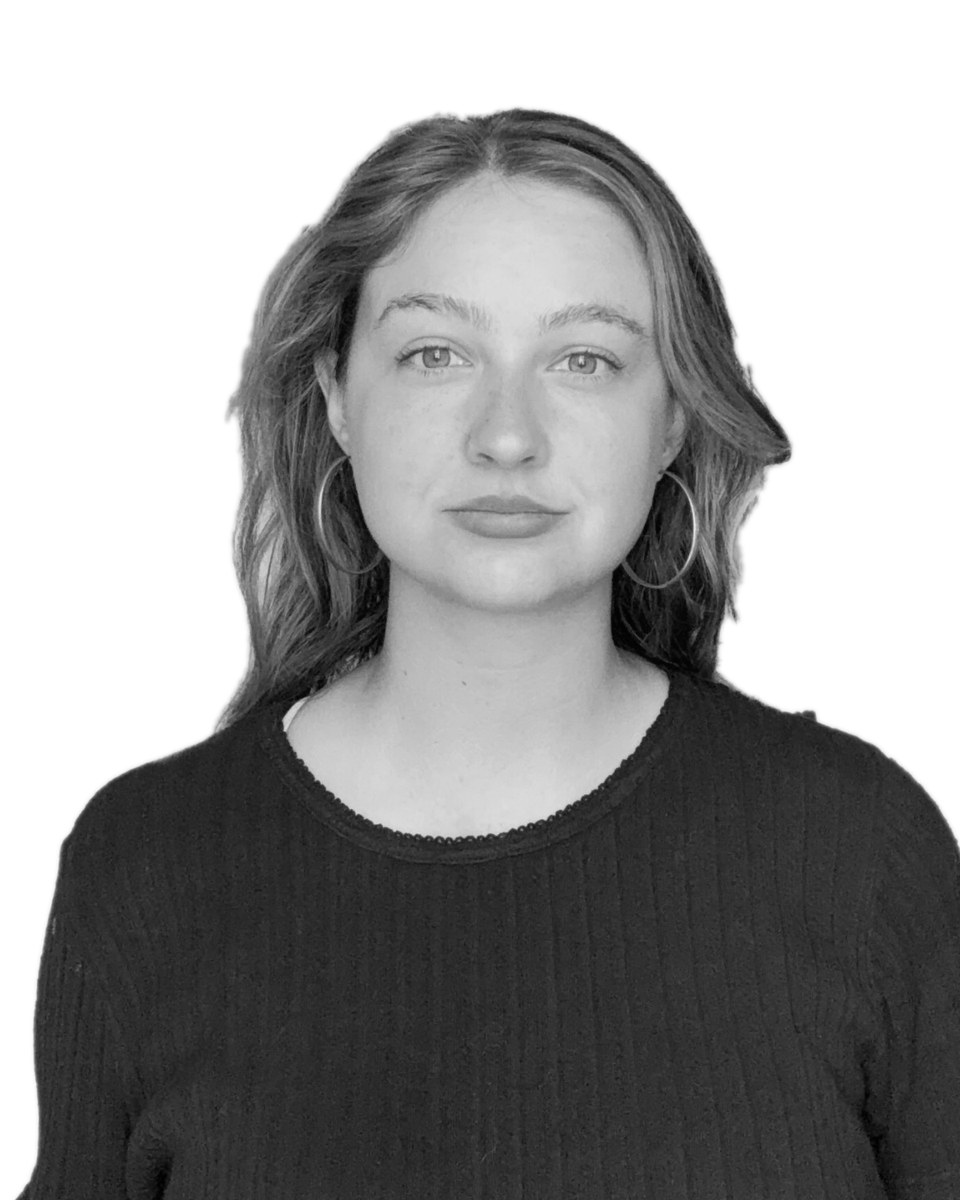 Black-and-white portrait of Sophia Collender in a dark top and hoop earrings, against a white wall.
