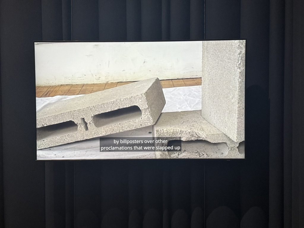 A cinder block projected on a dark wall with a caption quoting the novel.